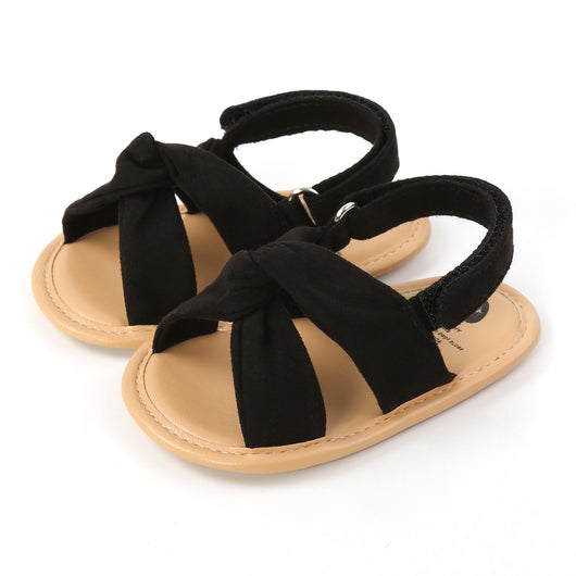 Black baby sandals with knotted cross straps and a matching black floral headband on a white background. - Image 21
