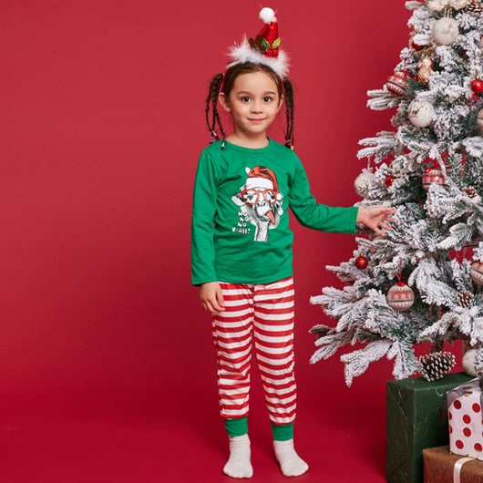 Child wearing green Christmas pajamas with a giraffe graphic and red striped pants, next to a flocked tree. - Image 12