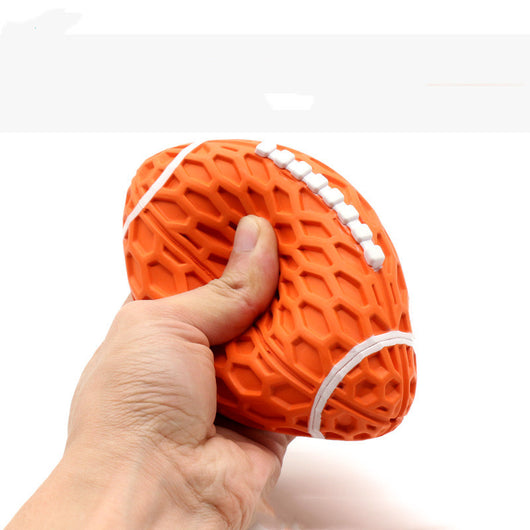 Orange rubber rugby ball dog toy with honeycomb texture and white laces, being squeezed by a hand. - Image 3