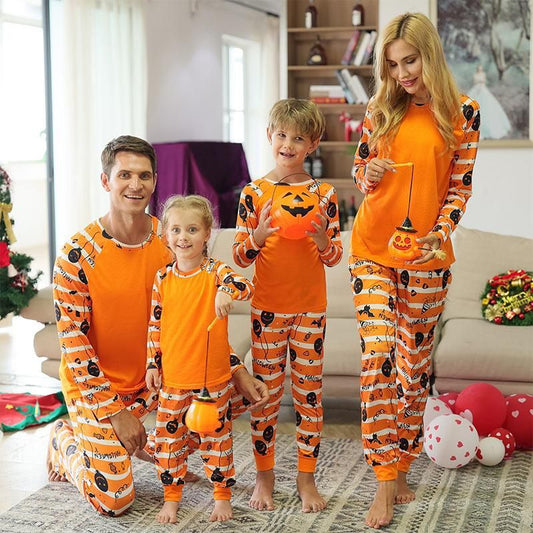 Family of four wearing matching orange and white striped Halloween pajamas with pumpkin and bat prints.