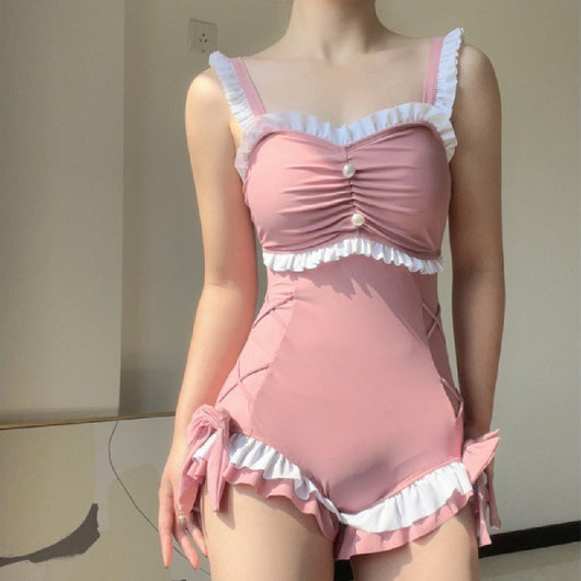 Pink one-piece swimming suit with white ruffles, ruched bust, pearl buttons, and shorts-style bottom with side ties.