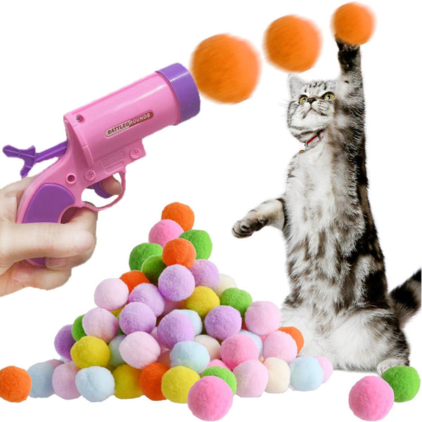 Pink pompom firing gun with a pile of colorful pompom balls and a cat playing with an orange ball.