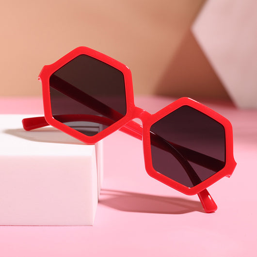 Red hexagonal children's sunglasses with dark lenses on a pink surface with a white block. - Image 6