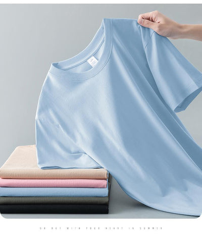 Light gray short-sleeve t-shirt with a round neck, held up to show its smooth fabric. A stack of folded t-shirts in various colors is visible in the background. - Image 22