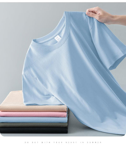 Light gray short-sleeve t-shirt with a round neck, held up to show its smooth fabric. A stack of folded t-shirts in various colors is visible in the background. - Image 22