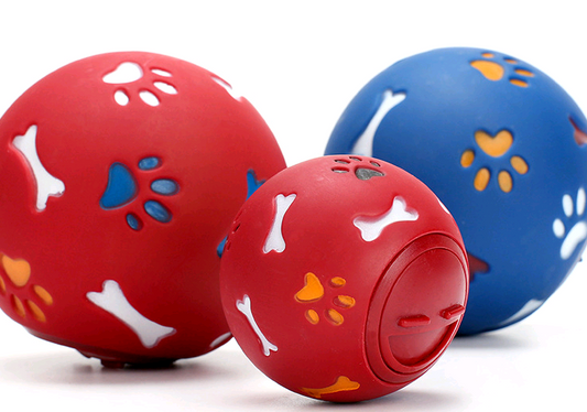 Red rubber pet puzzle ball with white, blue, and orange paw print and bone cutouts, featuring a treat dispenser opening. - Image 2