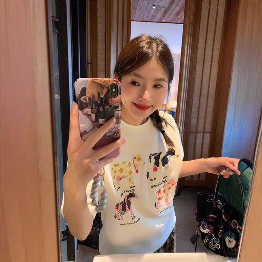 White loose-fit short-sleeve top with colorful retro cartoon cow print, modeled by a woman with plaid pants. - Image 3