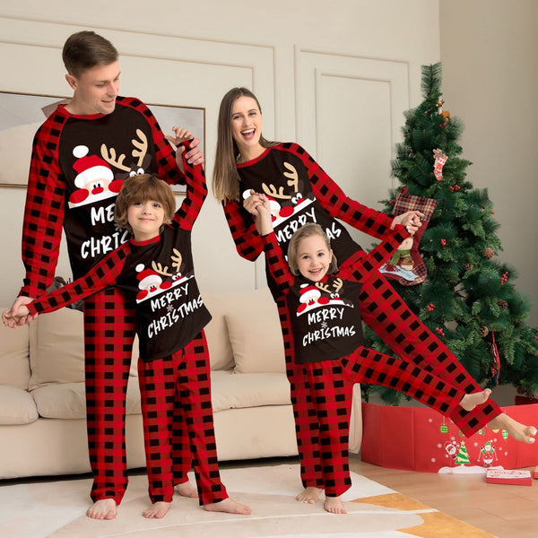 Family of four wearing matching red and black buffalo plaid Christmas pajamas with reindeer graphic.