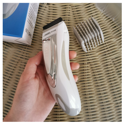 White and silver electric hair clipper held in hand, with a grey guide comb and blue packaging on a woven surface. - Image 15