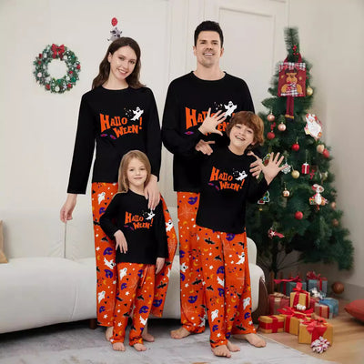 Family of four wearing matching black and orange Halloween long-sleeve pajamas with ghost and bat prints.
