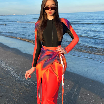 Woman in a black long-sleeve rash guard, black swim leggings, and a vibrant tie-dye sarong on a sunny beach. - Image 3