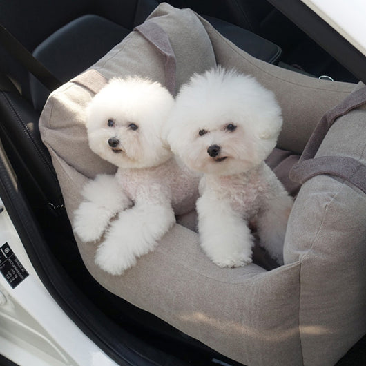 Beige pet car carrier seat with tan straps and a separate red pet seatbelt leash for safe car travel.