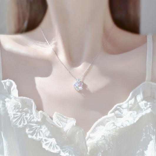 Gold-tone necklace with an iridescent camellia flower pendant and small clear stones on a delicate chain.