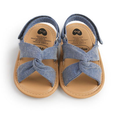 Black baby sandals with knotted cross straps and a matching black floral headband on a white background. - Image 9