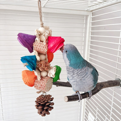 Blue parrot playing with a colorful natural material bird toy featuring corn cobs, wood, and pinecones, hanging in a white birdcage. - Image 4