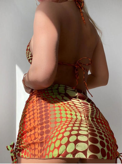 Women's printed split bikini swimsuit set with halter top, high-cut bottom, sarong skirt, and headscarf in green, brown, and orange optical dot pattern. - Image 8