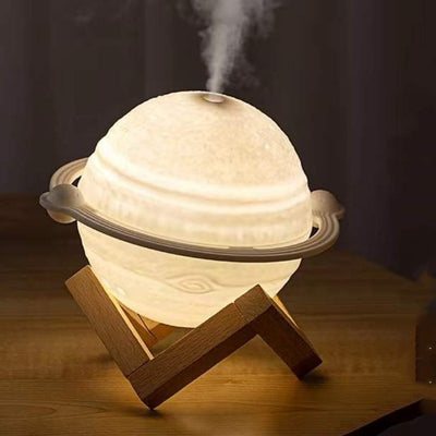 Yellow planet-shaped humidifier with a wooden stand emitting mist, next to a dark blue celestial gift bag. - Image 4