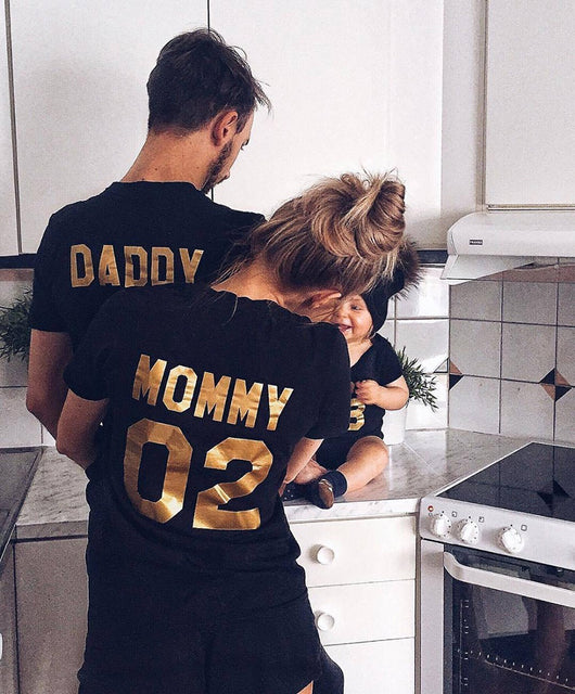 Child's black short-sleeved t-shirt with 'BABY 04' in gold print on the back, worn by a toddler in grass. - Image 3
