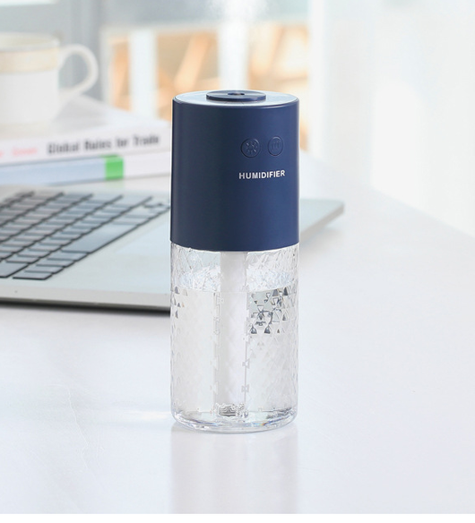 Dark blue and clear portable humidifier with a textured water tank on a white desk next to a laptop. - Image 12