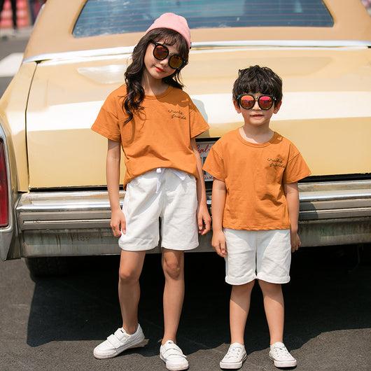 Family of four in matching khaki short-sleeved t-shirts and white shorts, posing outdoors with a vintage car. - Image 2