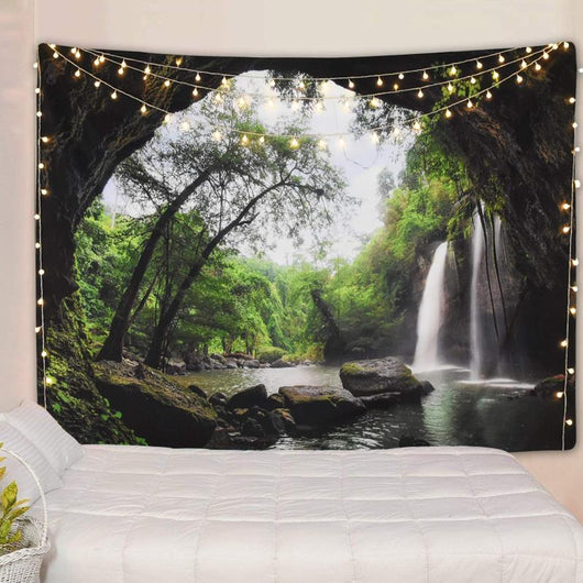 Cave waterfall print tapestry with lush green trees and dark rocks, adorned with warm string lights above a white bed. - Image 3