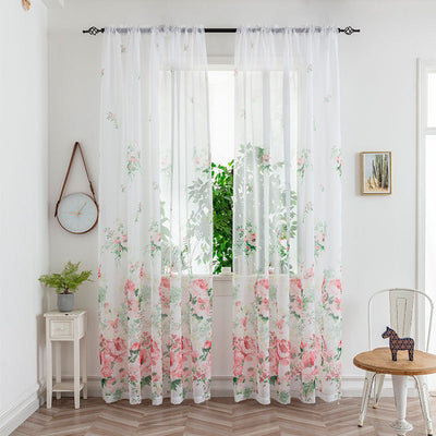 Sheer white mesh curtains with purple and light blue floral patterns, hung on a black rod in a bright room.