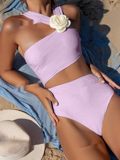 Light purple one-shoulder swimsuit with a 3D white flower detail, worn by a person lounging on a beach. - Image 6