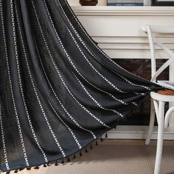 Black polyester curtain with white jacquard multi-line pattern and black tassels, draped over a white chair.