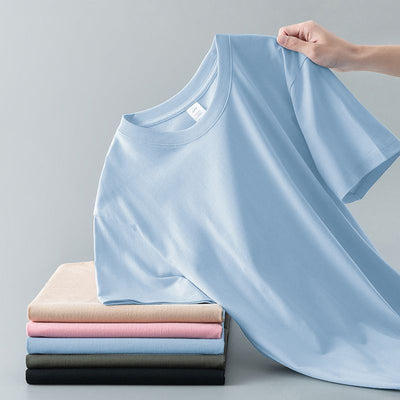 Light gray short-sleeve t-shirt with a round neck, held up to show its smooth fabric. A stack of folded t-shirts in various colors is visible in the background. - Image 7