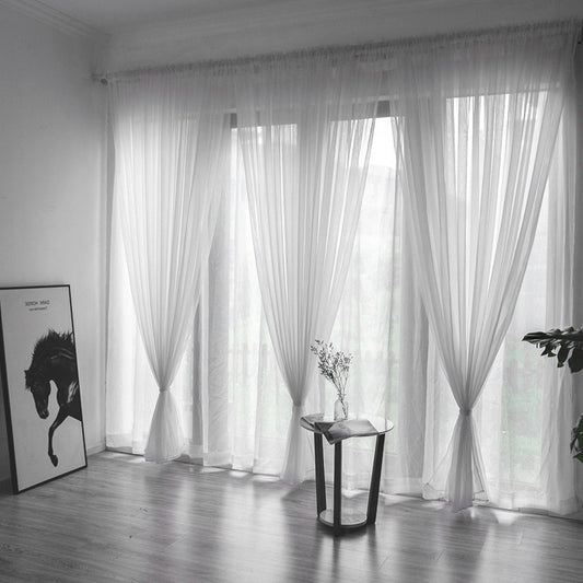 Pair of sheer blue polyester curtains for light transmission, ready-made and punch-free, hanging in a window.