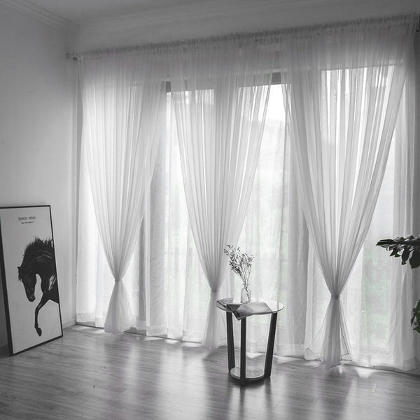 Pair of sheer blue polyester curtains for light transmission, ready-made and punch-free, hanging in a window.