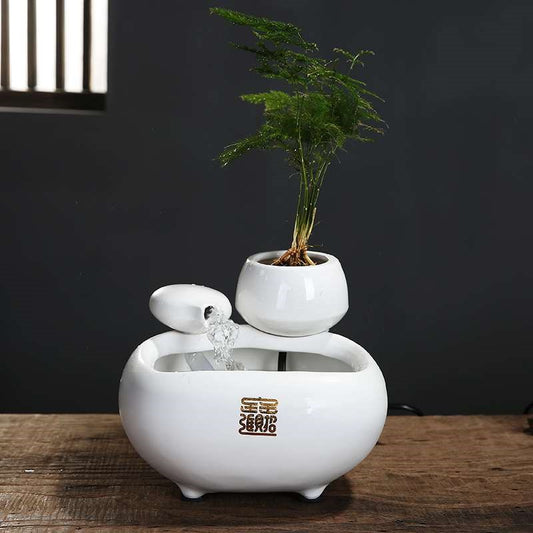 White ceramic flowing water fountain ornament with an integrated planter holding a green plant. Features gold Chinese characters.