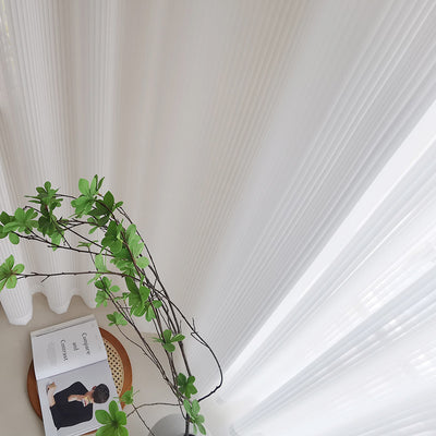 White vertical blinds with a pleated texture, allowing sunlight to filter through and cast shadows on an open magazine. - Image 2