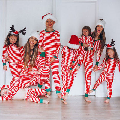 Family of four wearing matching red and white striped Christmas pajamas with green cuffs. One child wears a Santa hat, another wears reindeer antlers.