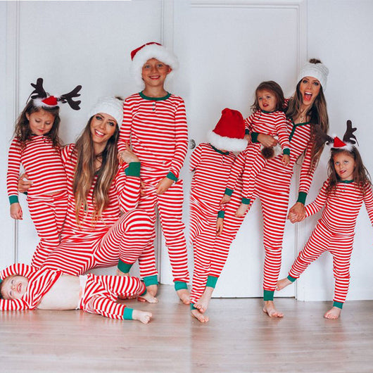 Family of four wearing matching red and white striped Christmas pajamas with green cuffs. One child wears a Santa hat, another wears reindeer antlers.