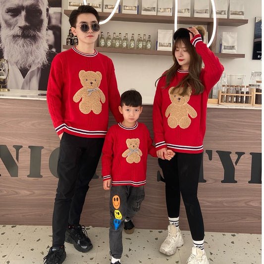 Family of three wearing matching red cable-knit sweaters with a brown teddy bear appliqué and striped trim. - Image 2