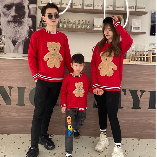 Family of three wearing matching red cable-knit sweaters with a brown teddy bear appliqué and striped trim. - Image 2