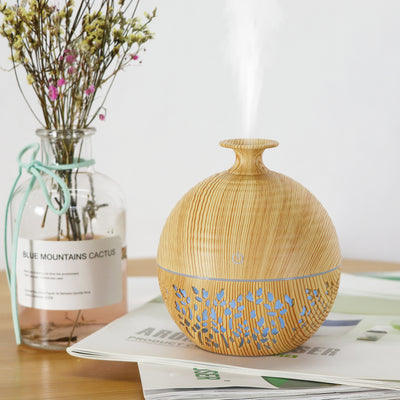 Light wood grain portable mini aroma diffuser humidifier with a vase shape and glowing blue leaf patterns.