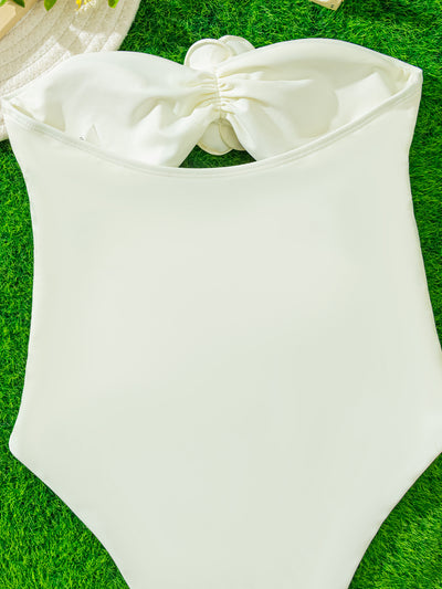 White strapless one-piece swimsuit with 3D flower details and side cut-outs, worn by a woman by an infinity pool. - Image 3
