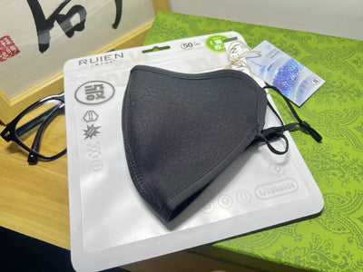 Dark gray cotton head-mounted mask with adjustable ear loops, shown in packaging on a patterned green surface. - Image 9