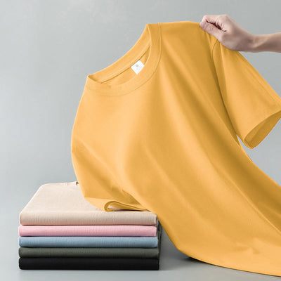 Light gray short-sleeve t-shirt with a round neck, held up to show its smooth fabric. A stack of folded t-shirts in various colors is visible in the background. - Image 12