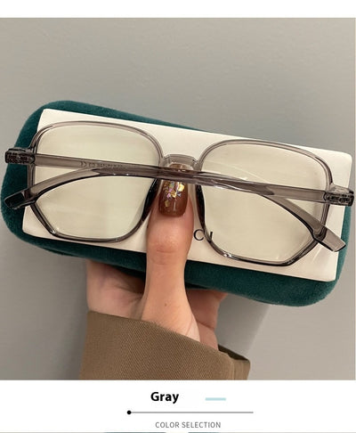 Mocha brown irregular frame glasses with clear lenses, held over a dark green velvet glasses case. - Image 13