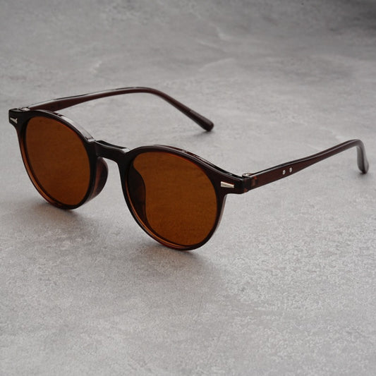Fashionable round-frame sunglasses with transparent gray frames and dark gray lenses on a gray surface. - Image 2
