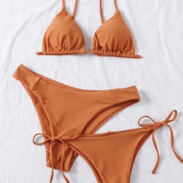 Lavender three-piece bikini set with a triangle top, tie-side bottom, and high-cut bottom, displayed with a straw hat and purple sunglasses.