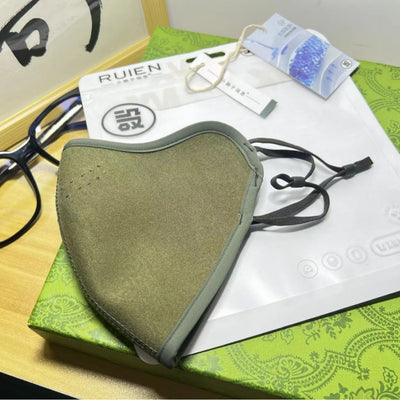 Dark gray cotton head-mounted mask with adjustable ear loops, shown in packaging on a patterned green surface. - Image 2