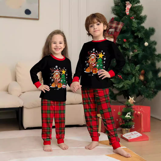 Two children in black and red plaid Christmas pajamas with a reindeer and Christmas tree graphic, standing by a Christmas tree. - Image 2