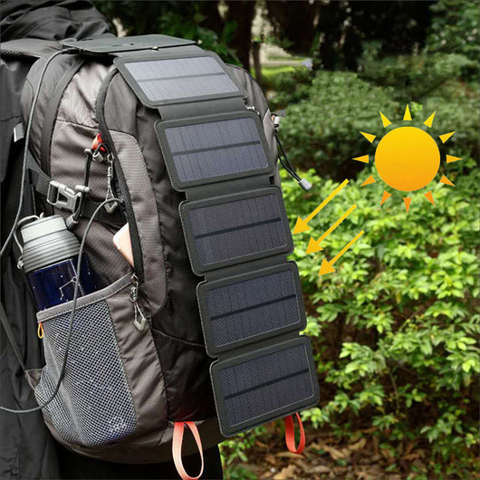 Black portable folding solar panel charger with six panels attached to a backpack in an outdoor setting.