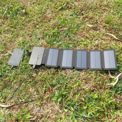 Black portable folding solar panel charger with six panels attached to a backpack in an outdoor setting. - Image 9