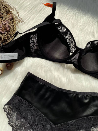 Black lace and smooth fabric bra and matching panties set, featuring a decorative ring, on a white faux fur surface. - Image 2