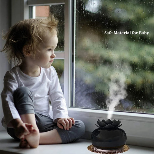 Black spherical aromatherapy humidifier with a lotus flower top, emitting mist, sitting on a gold decorative doily. - Image 13